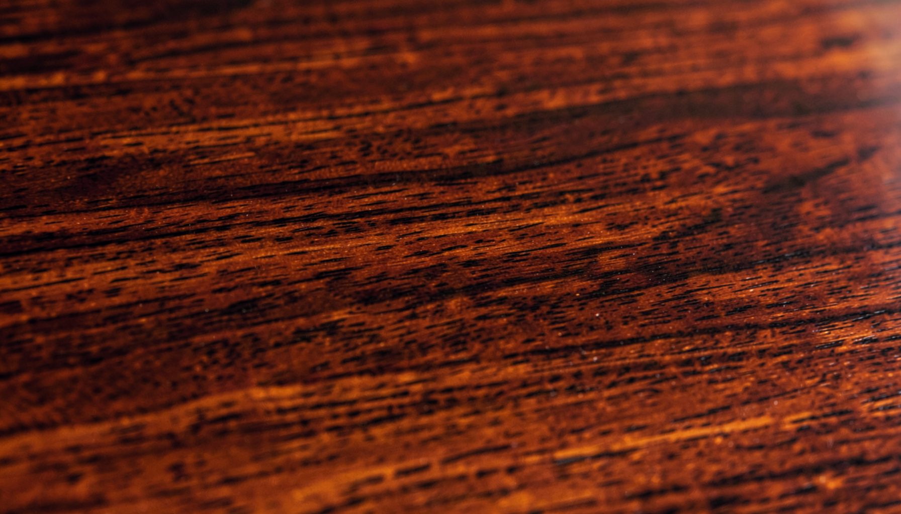 Close-up of rich mahogany wood grain with deep reddish-brown tones and a subtle gloss, warm and elegant