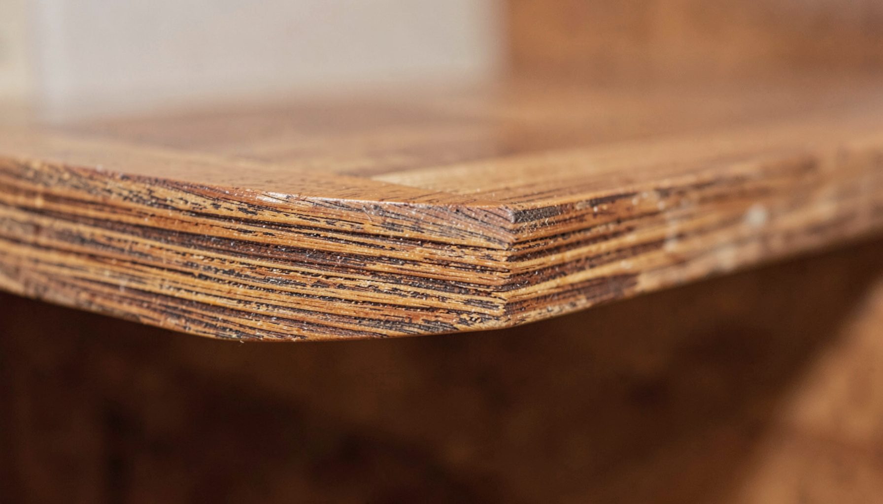 Close-up of wood furniture edge showing layered construction, warm brown tones with visible grain detail