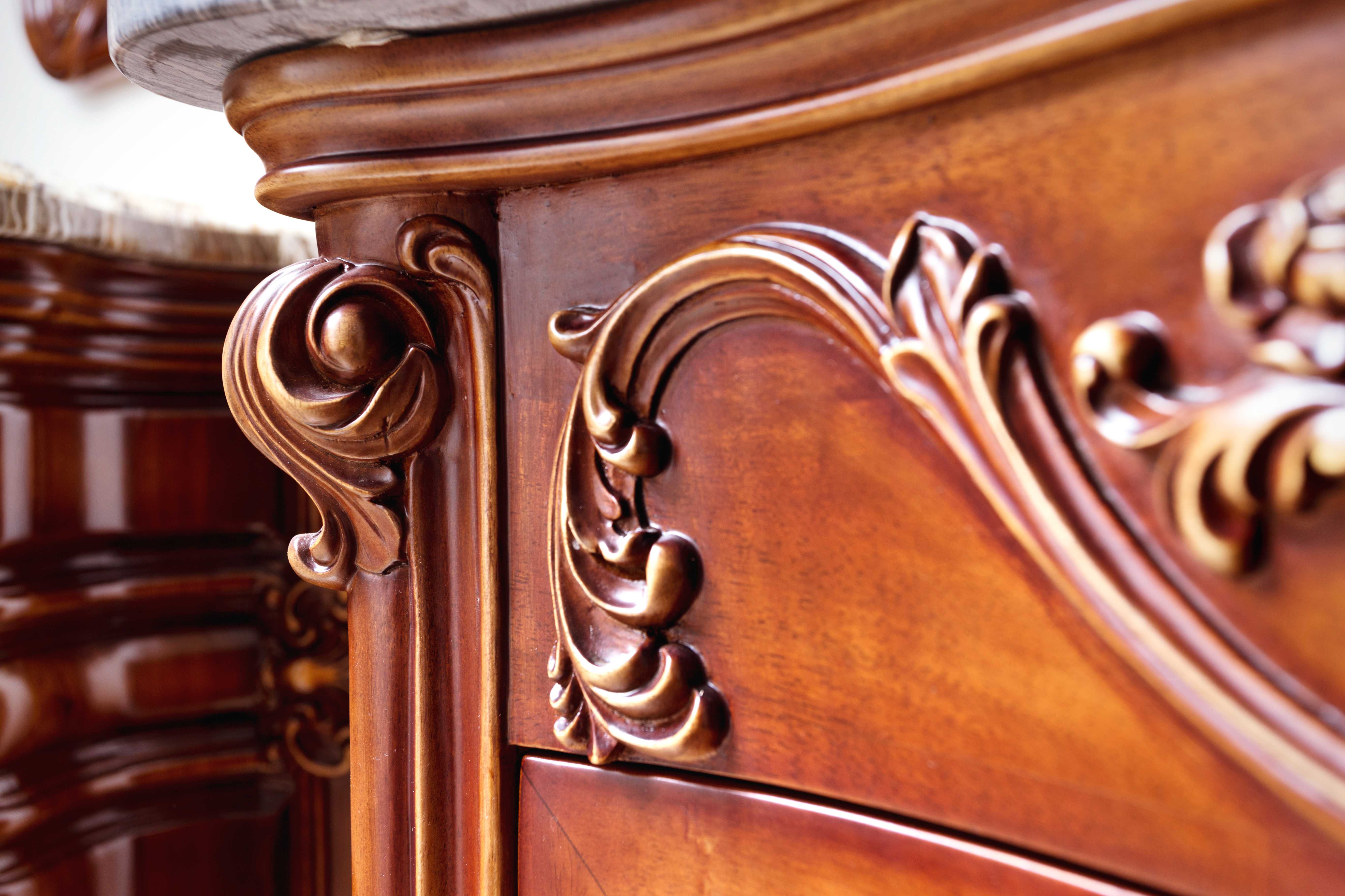 Close-up of richly carved wooden furniture with flowing scroll and leaf motifs in warm brown tones